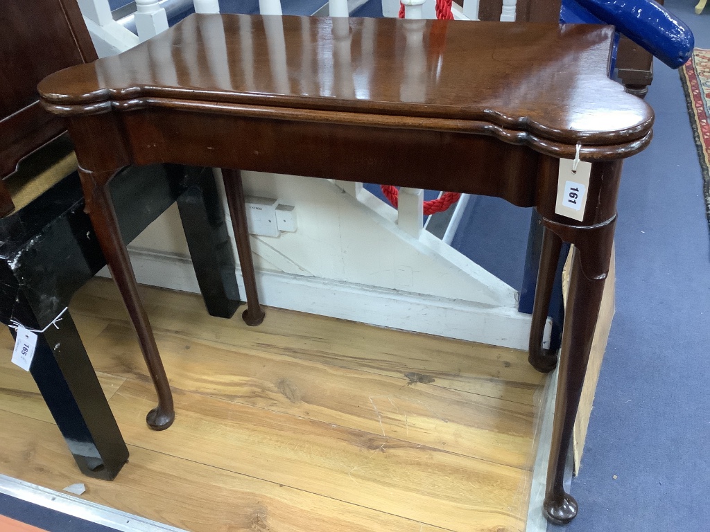 An 18th century mahogany games table, having shaped folding top enclosing counter wells and leather-lined surface on lappet-carved legs and pad feet, width 86cm depth 42cm height 72cm